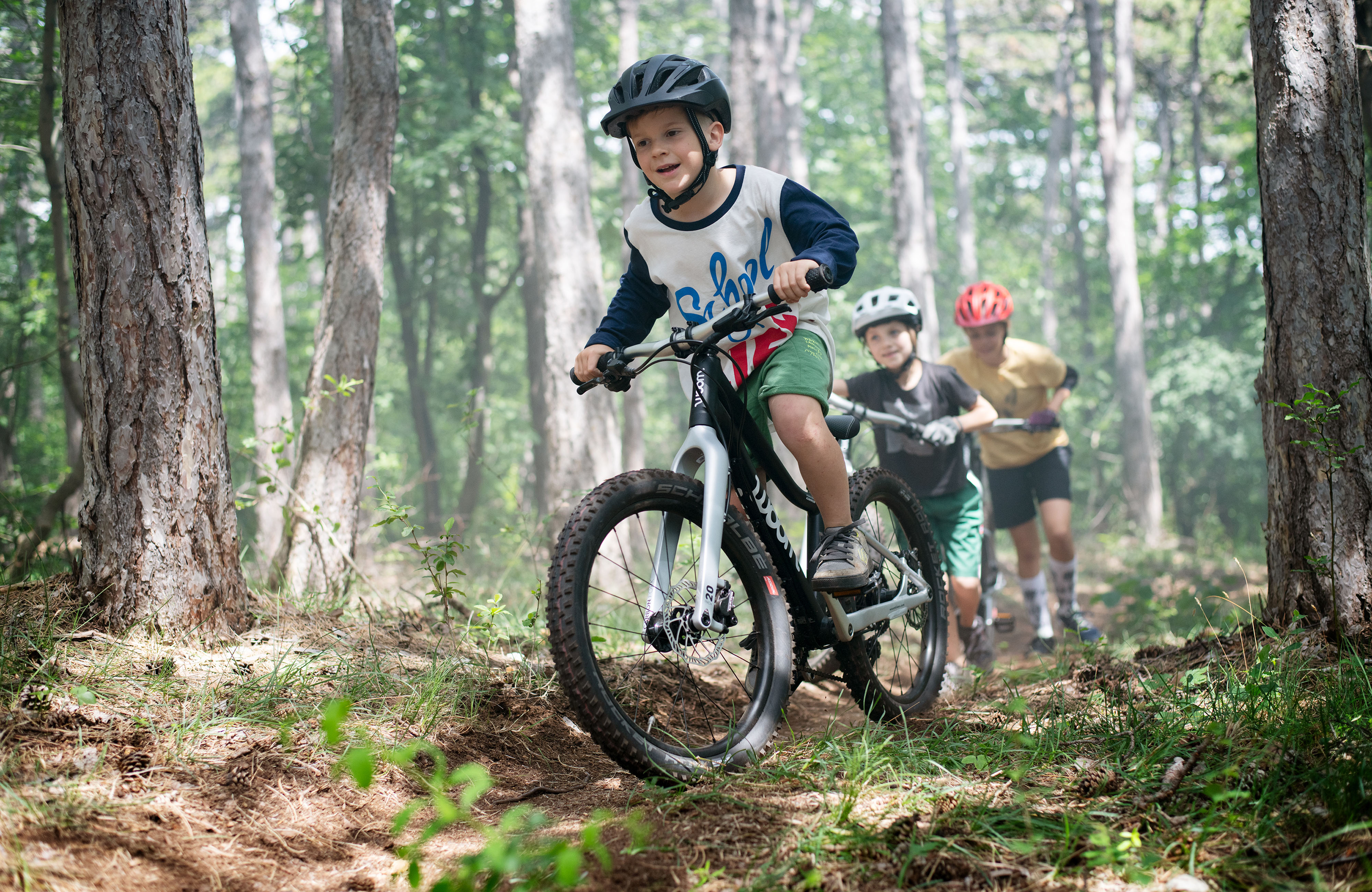 Drei Kids sind mit Woom OFF im Wald bergauf unterwegs-4000x2600px